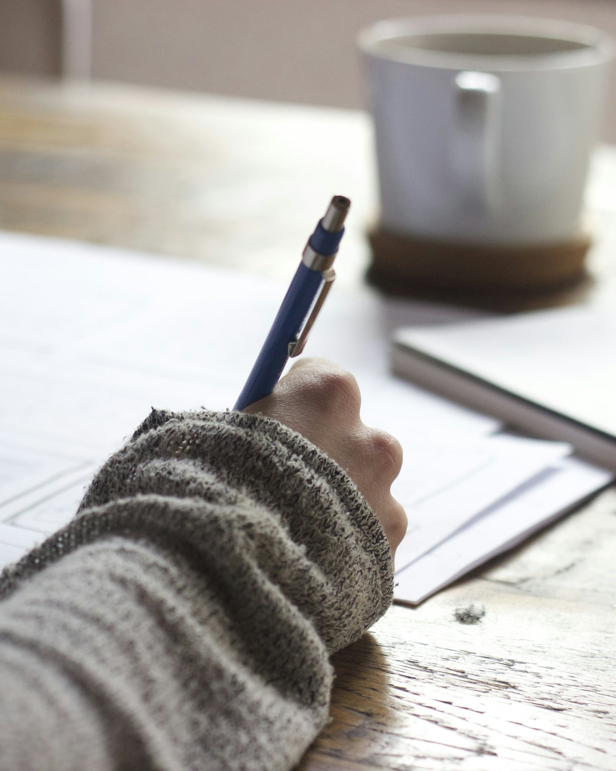 Main qui prend des notes sur une feuille, près d’une tasse de café