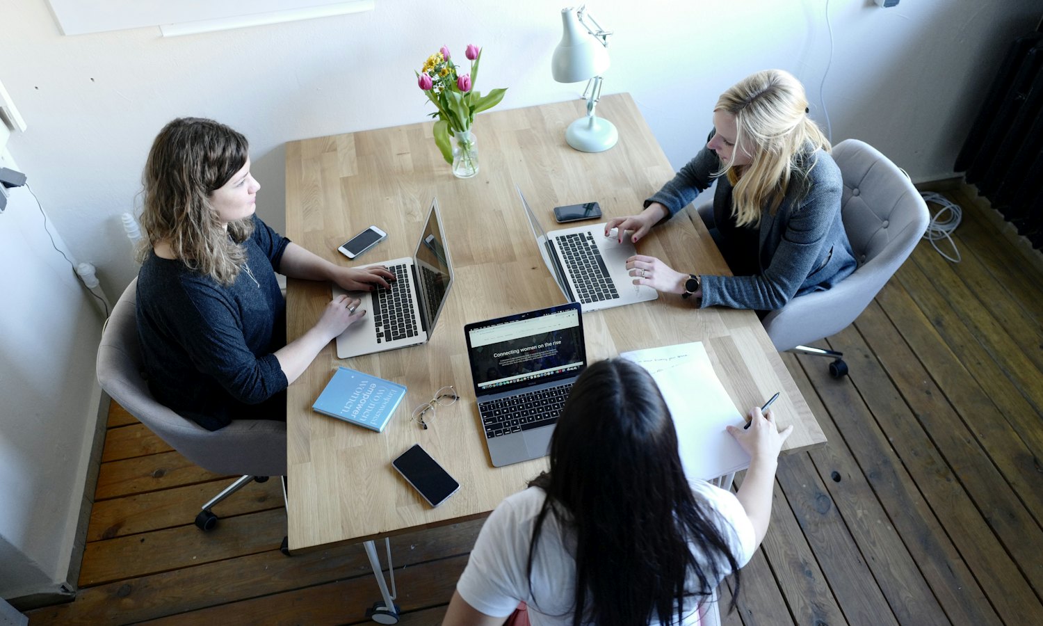 Trois femmes qui travaillent autour d’une table de bois clair, vues d’en haut