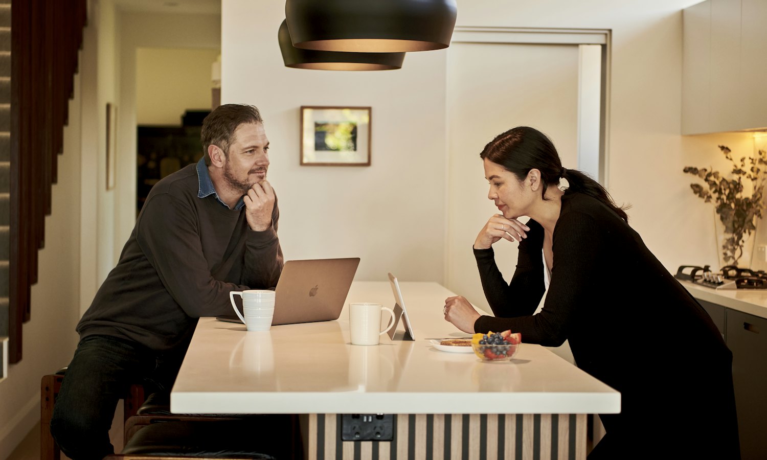 Un homme et une femme qui réfléchissent ensemble, le menton dans la main, à un comptoir de cuisine