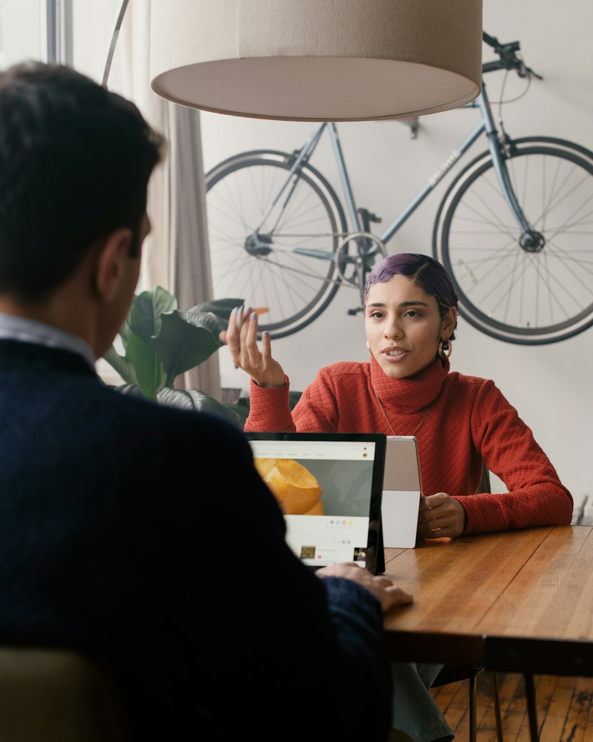 Femme qui explique calmement quelque chose à un collègue devant un ordinateur portable, à une table de bois