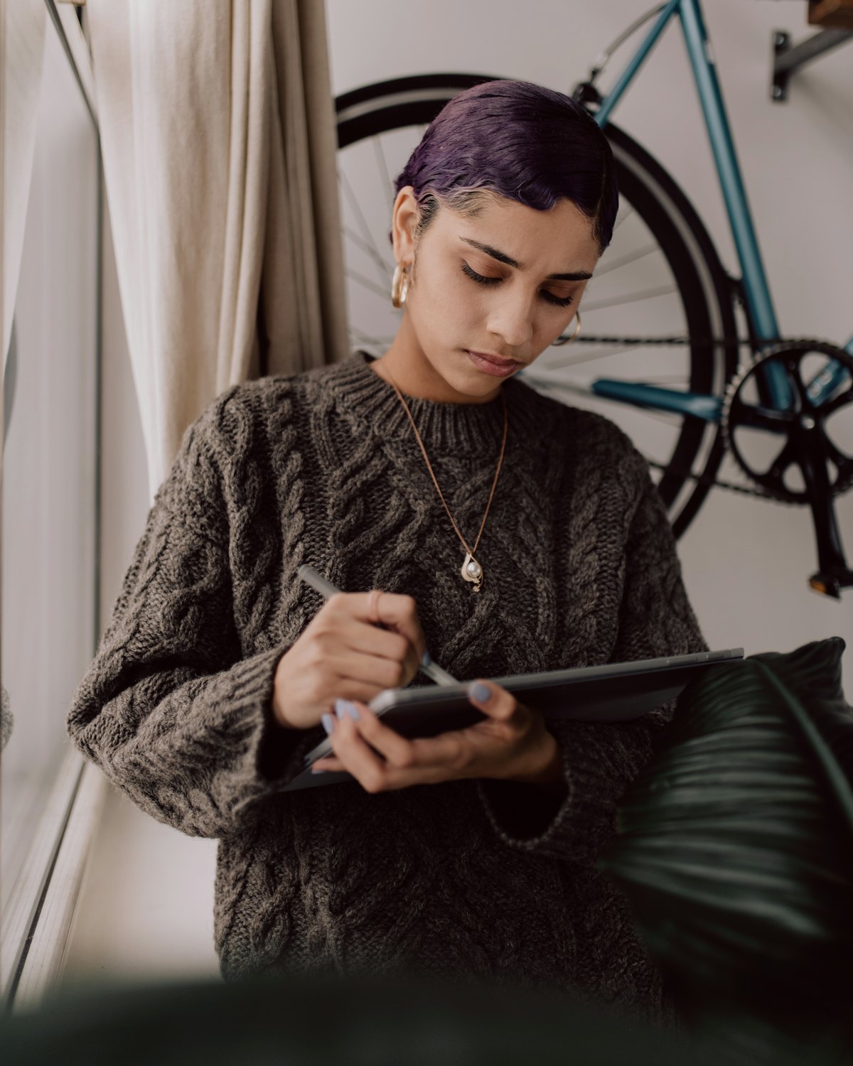Femme concentrée qui écrit sur une tablette, en pull de laine, près d’une fenêtre