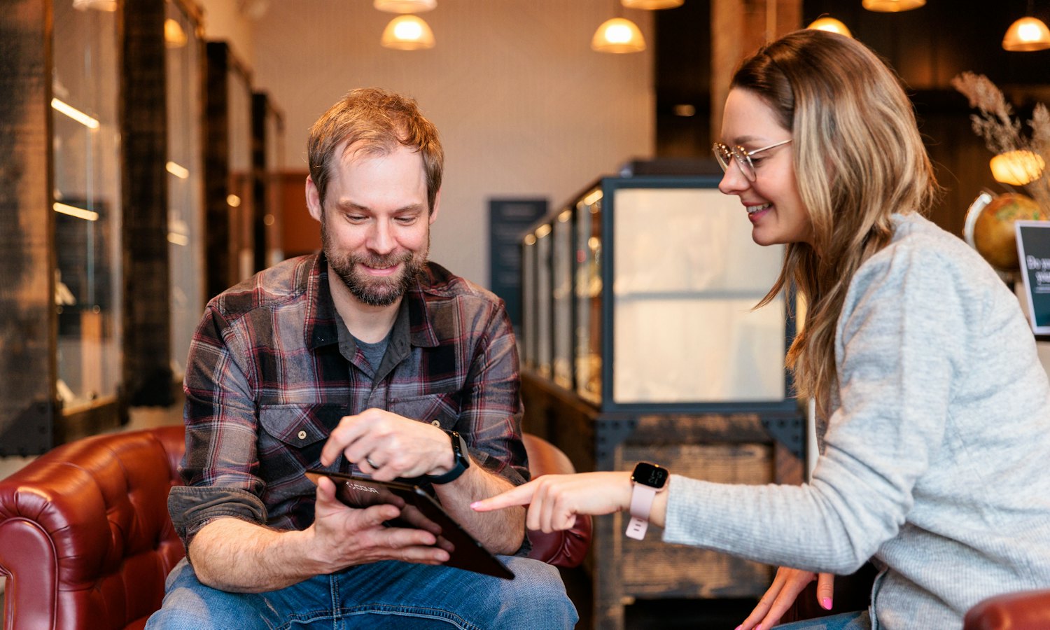 Un homme et une femme assis dans une boutique chaleureuse, qui regardent ensemble une tablette, la femme pointe l’écran