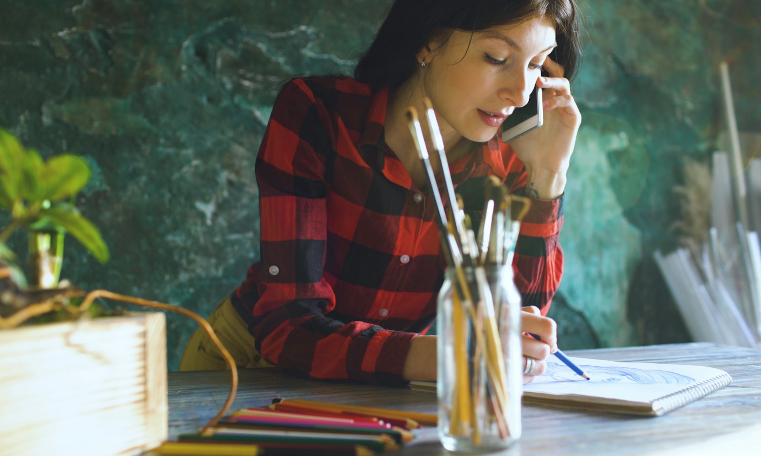 Femme qui répond au téléphone à sa table, un carnet de croquis et des crayons devant elle